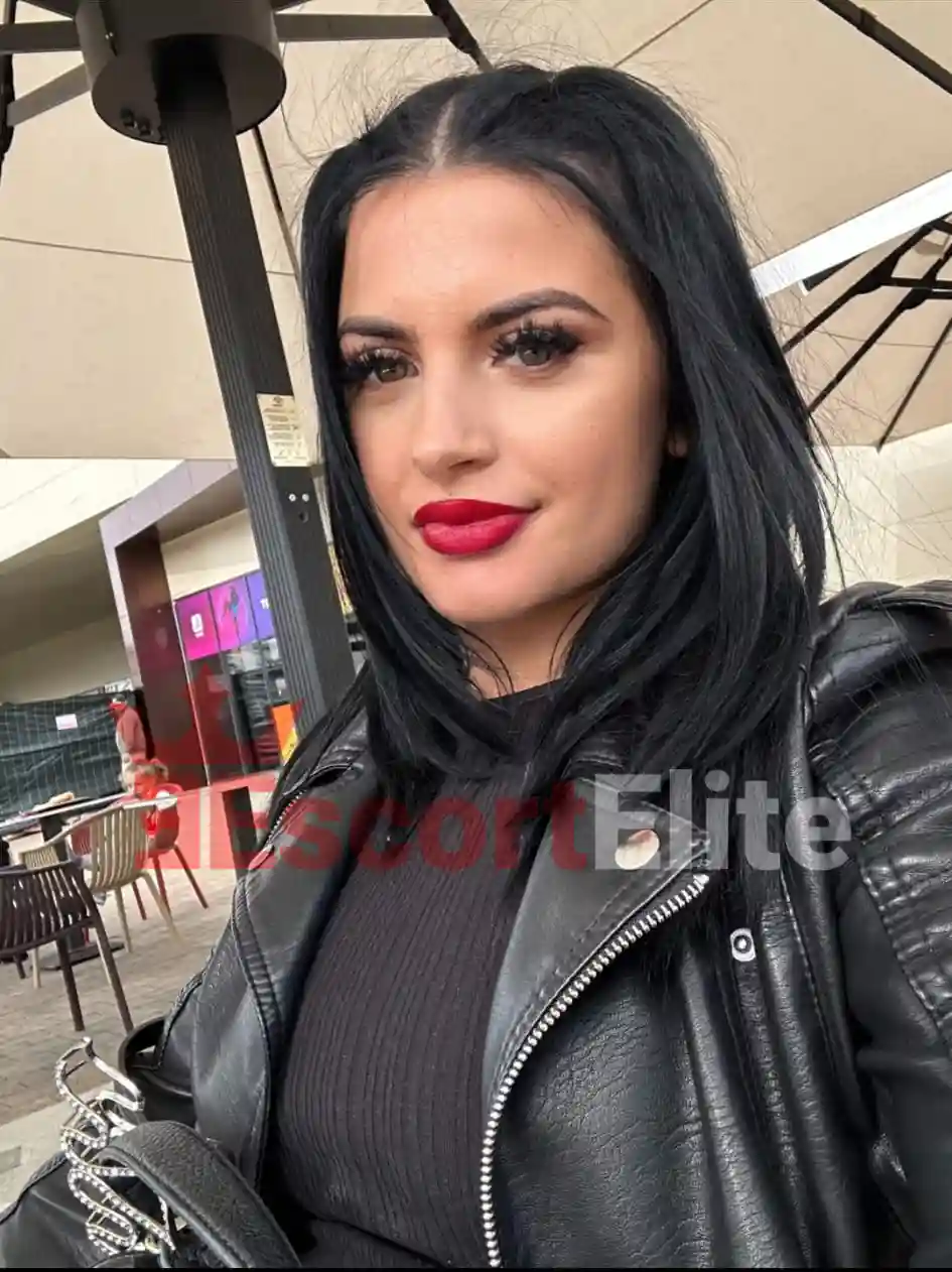 Alessia Wien Lederjacke rote Lippen Outdoor Alessia Premium Escort Wien Nahaufnahme-Selfie in schwarzer Lederjacke mit roten Lippen auf einer Caféterrasse