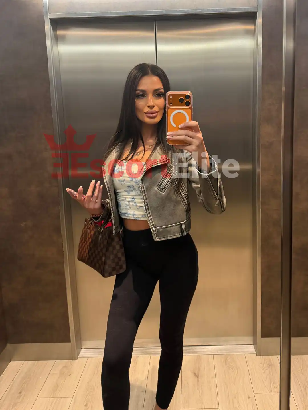 Escort Wien Kassandra im legeren Chic-Look mit Lederjacke, Spiegelselfie im Fahrstuhl