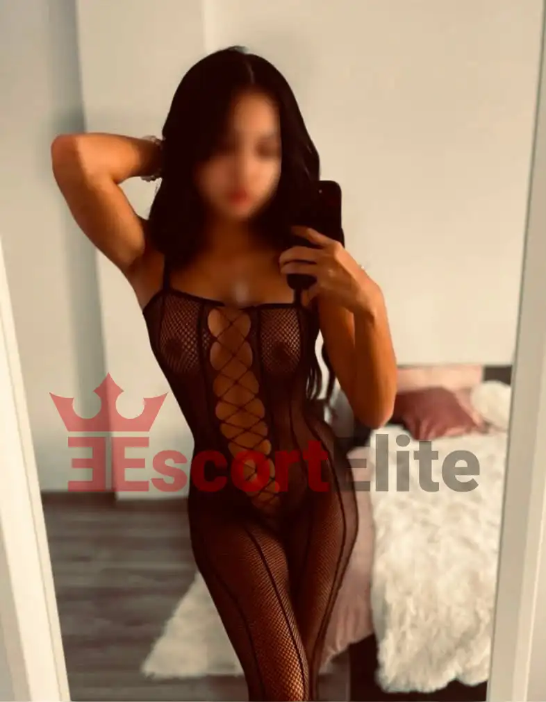 Mely Viena – Retrato sensual en rejilla Joven escort Mely Viena en mono de rejilla negro con el brazo levantado en el cabello, retrato sensual en el dormitorio