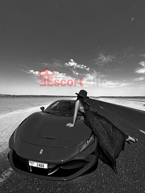 Escort Vienne Rossa en robe élégante sur une voiture de sport – photo noir et blanc